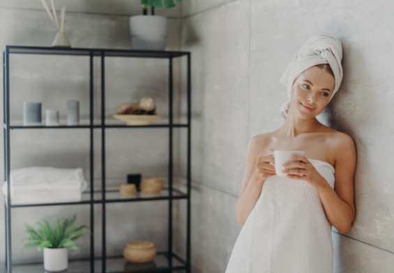 Calm relaxed woman poses in towel against bathroom interior, wrapped in bath towel